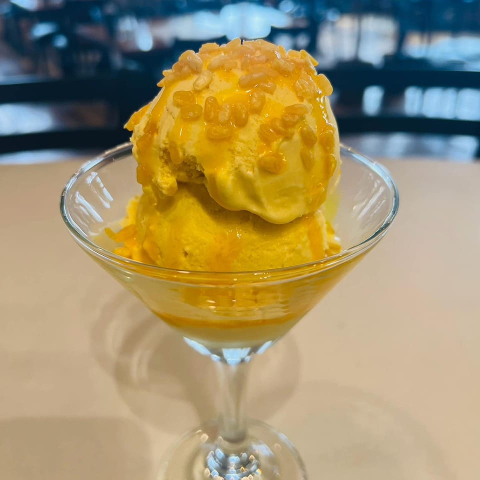 Two scoops of mango ice cream topped with syrup and crispy rice in a martini glass.