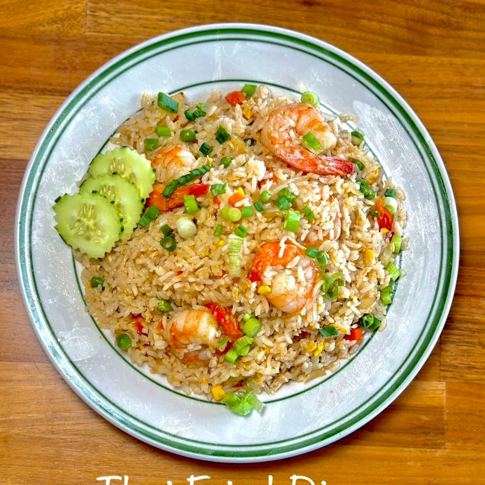 Thai fried rice with shrimp, green onions, peas, and cucumber slices on a white plate.