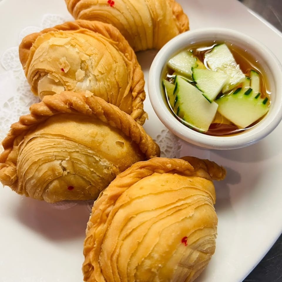 Golden-brown Thai curry puffs with a side of cucumber relish on a white plate.