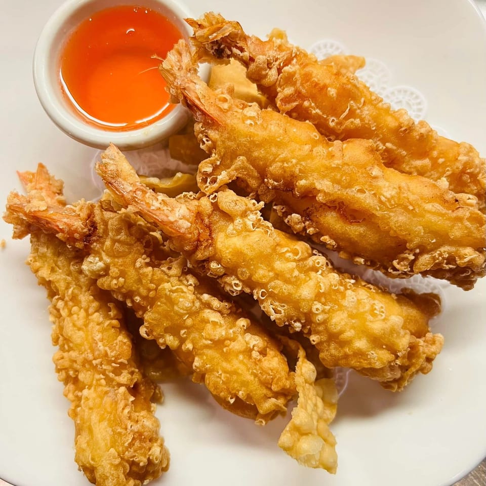 Crispy fried shrimp tempura with a side of sweet chili dipping sauce on a white plate.