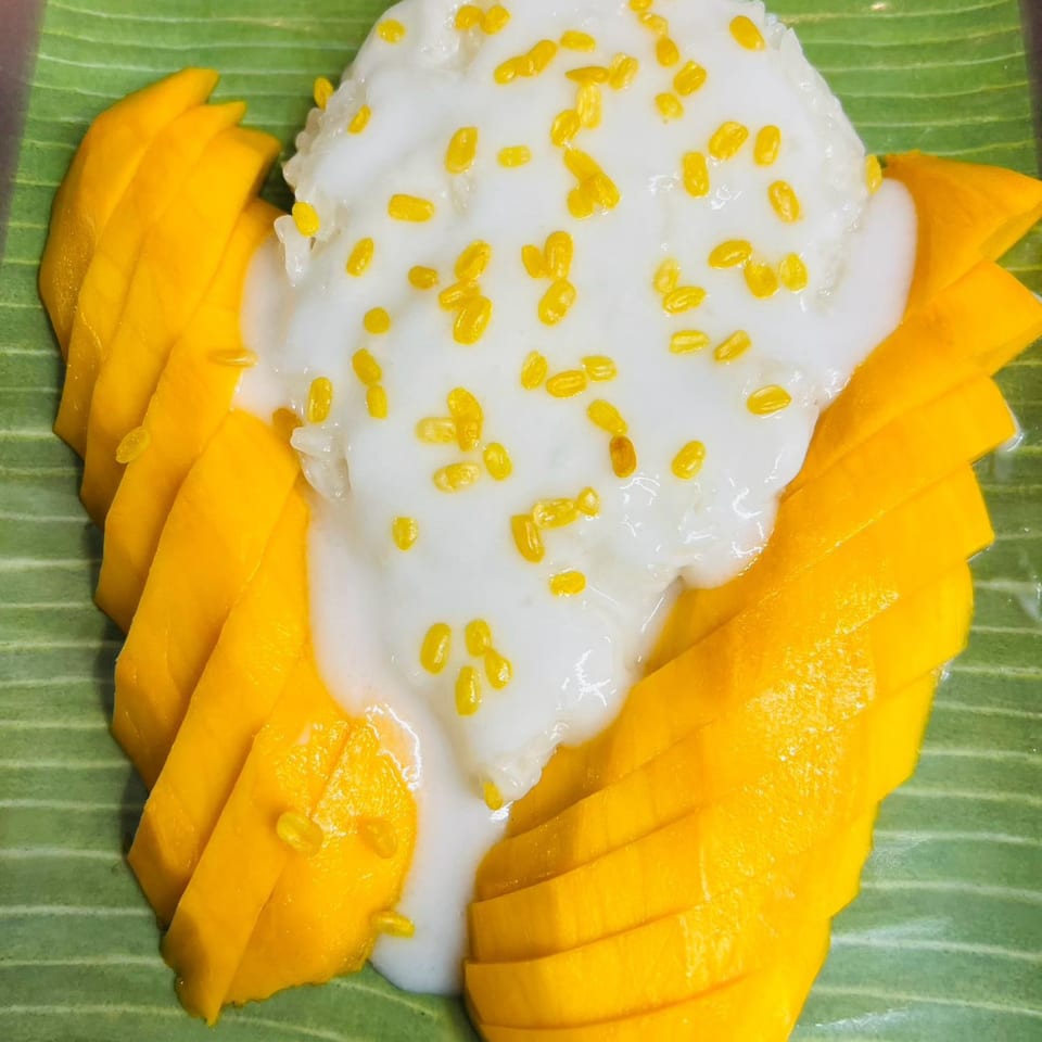Mango sticky rice with coconut milk and yellow mung beans on a green banana leaf.